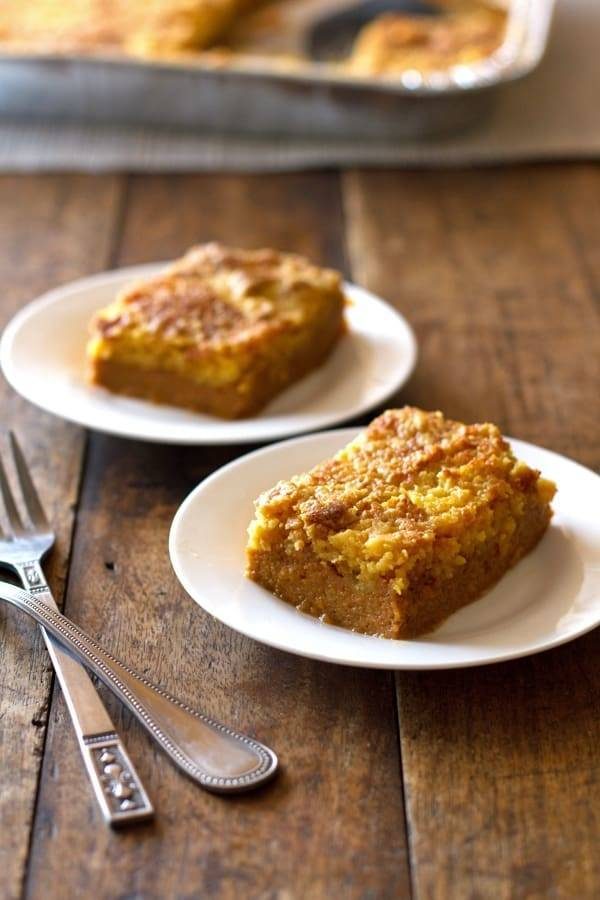 Two pieces of pumpkin dessert bars on white plates.