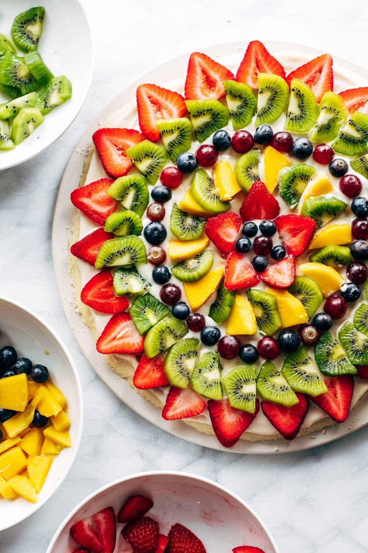 Fruit pizza with bowls of fruit.